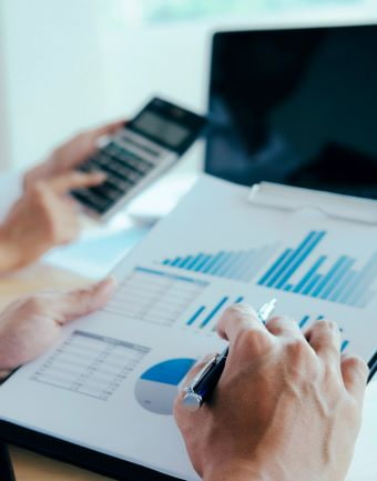 rozmyte zdjęcie komuter, kalkulatror, kartki z wykresami, na pierszym planie dłoń z długopisem