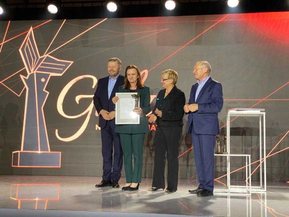 Prof. Gertruda Uścińska stoi na scenie obok innych uczestników panelu. w ręku trzyma nagrodę.