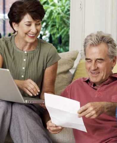 para starszych osób, wyżej siedzi usmiechnięta kobieta z laptopem, poniżej mężczyzna z kartką w ręce, zgięta jak pismo wyjete z koperty
